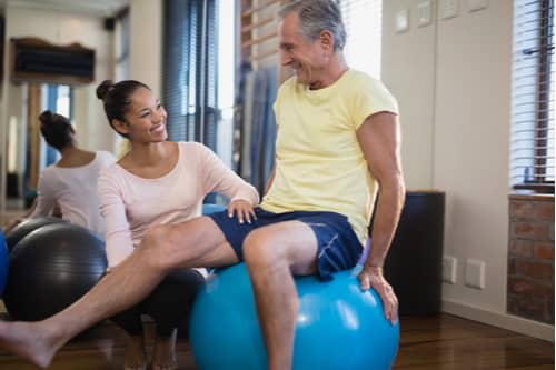 Female physical therapist helping senior man use exercise ball, Fort Myers physiotherapy services